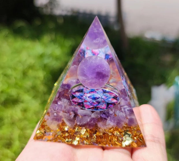 Hand holding an amethyst orgone pyramid with crystal sphere and colorful geometric design