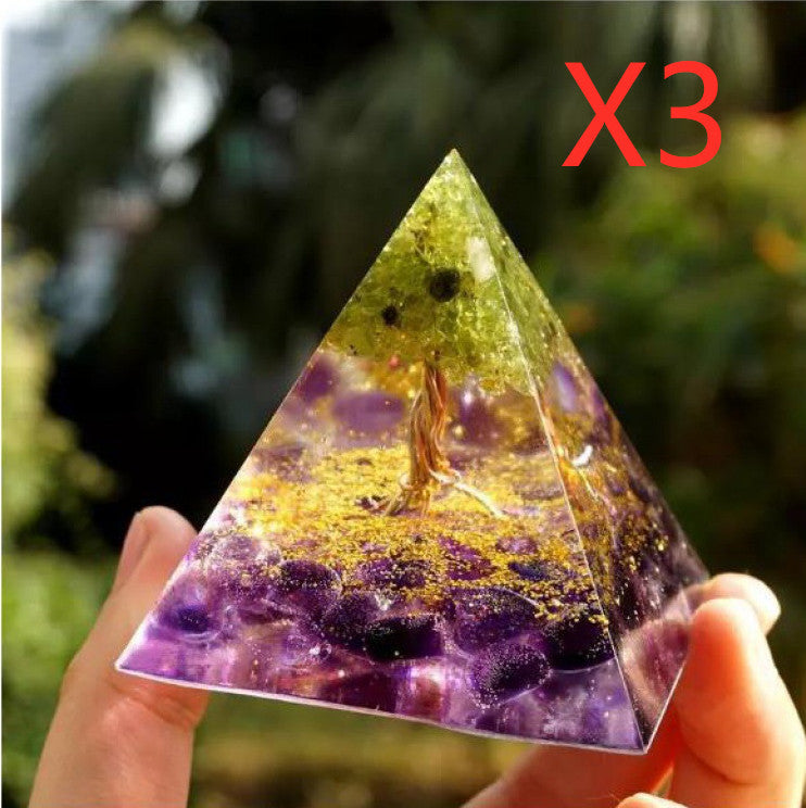 Hand holding a resin orgonite pyramid with purple stones, gold flecks, and tree design, outdoors